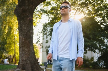 Young handsome blinded man walking with stick in town