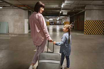 Attractive lady with her child and travel suitcase, searches for their car before starting trip....