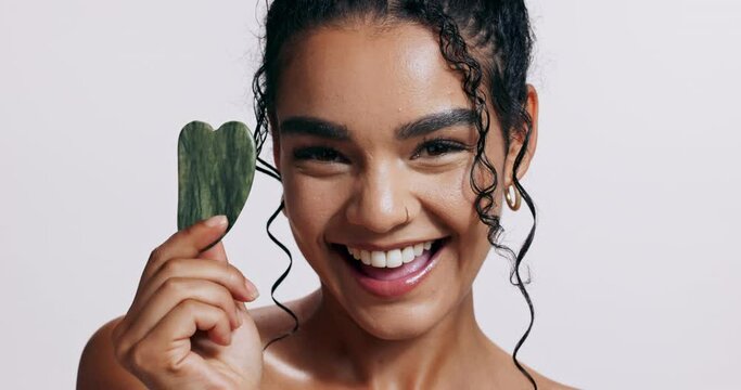 Skincare, gua sha and portrait of woman with facial massage, beauty and happiness in studio. Excited, smile and jade face tool for self care, smooth skin and dermatology treatment on white background