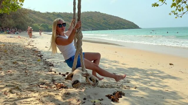 Blonde woman sitting on swings on a beach at the seaside on a sunny day