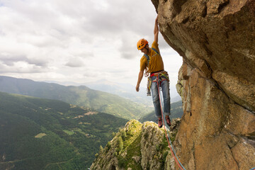 A man is climbing a rock wall with a yellow shirt and an orange helmet. The scene is set in a...