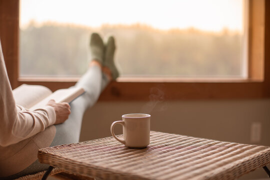 woman sitting reading while drinking hot tea. Young brunette woman thinking at home enjoying leisure time. Happy girl relaxing at home on a bright winter morning.