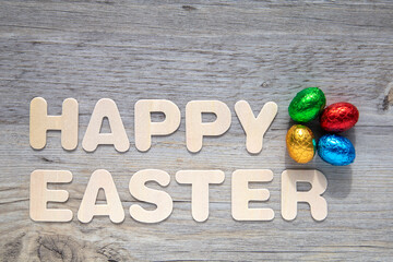 Foil covered Easter eggs on wooden background with the text "Happy Easter".
