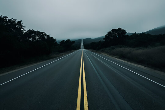 A desolate stretch of road cutting through a misty forest at dusk