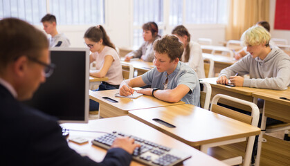 Fototapeta premium Smart teenager studying in classroom, listening to lecturer and writing in notebook..