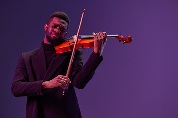 Elegant musician performing classical music on violin in black suit against vibrant purple backdrop