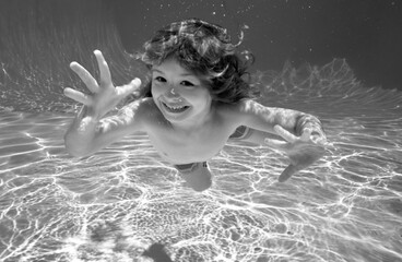 Child underwater. Funny face portrait of child boy swimming and diving underwater with fun in pool.
