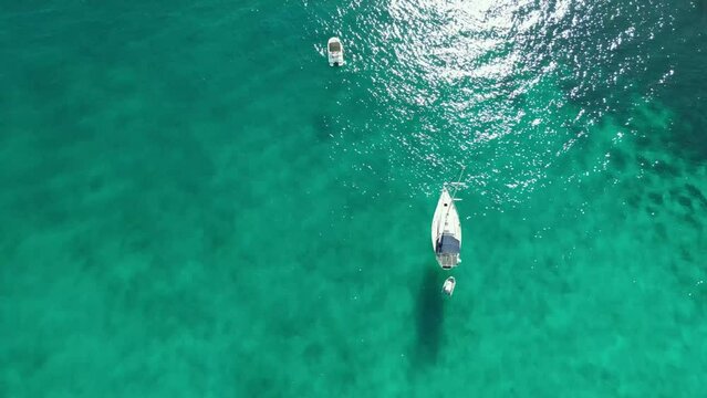 toma cenital &aacute;rea con dron de un yate fondeado en las transparentes aguas del mar mediterr&aacute;neo en Mallorca. El dron sube lentamente abri&eacute;ndose el campo de visi&oacute;n.