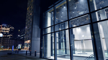 Night view on the ground floor of modern office building with big glass windows and entrance. Street reflection.