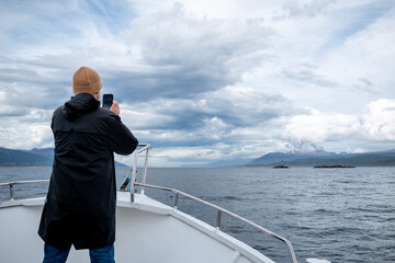 Turista navegando por el canal de Beagle, parado en Proa y tomando fotos con su celular	