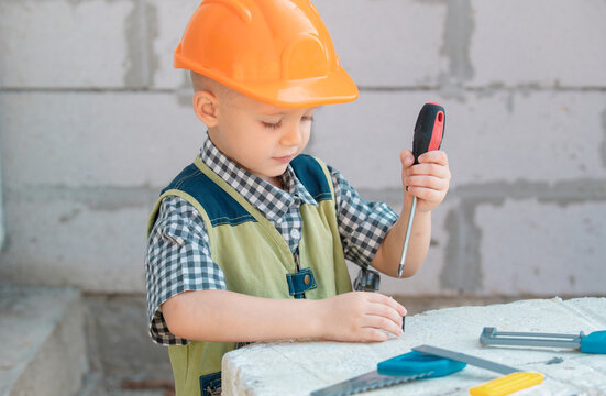 Little boy holding screwdriver. Kid twists bolt with screwdriver. Little Repairman with repair tool. Cute kid as a construction worker. Childrens play with a hammer pliers and screwdriver.