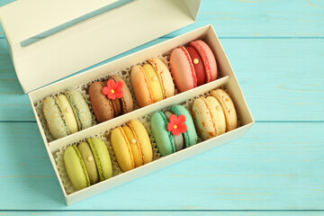 Multi-colored pasta in a white cardboard box standing on a light blue wooden background. Closeup