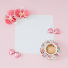 Fototapeta na wymiar Creative trendy layout made with cup of coffee, orchid flowers, pink foil wrapped chocolate hearts and paper card note copy space on light pink background. Minimal concept. Flat lay.