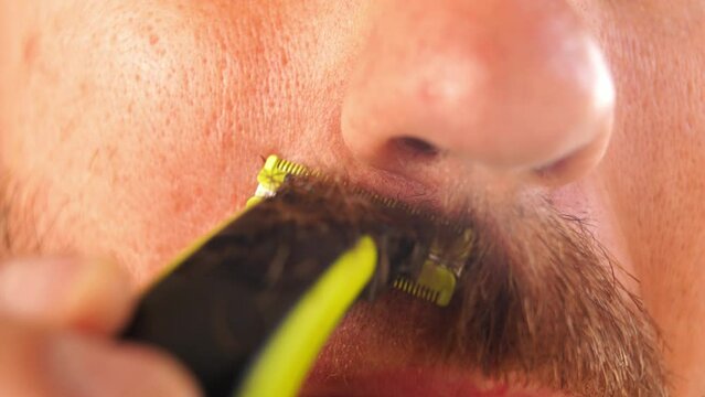 Man shaves his mustache with a trimmer. Portrait. Cropped. High quality 4k footage