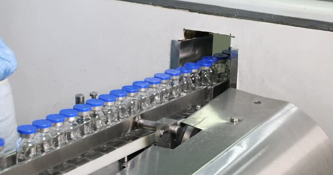 vaccine injection vials moving on a conveyor belt, filled with liquid medication, veterinary vaccines production in a pharmaceutical drug manufacturing factory, making medicine