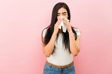 Sick latin woman blowing her nose suffering from a cold