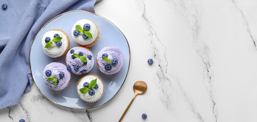 Plate of delicious cupcakes with blueberries and mint on white background