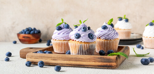 Wooden board of delicious cupcakes with blueberries and mint on white background