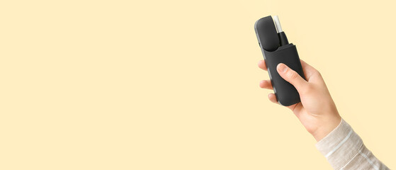 Female hand holding modern electronic cigar with stick on beige background