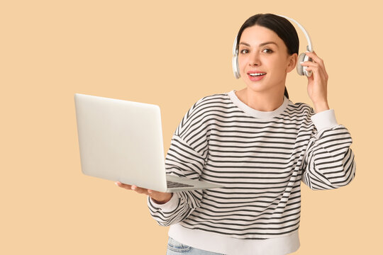 Female programmer in headphones with laptop on beige background