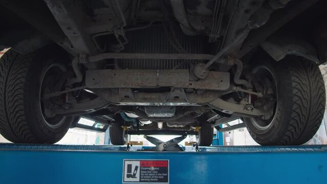 Camera span under suspended car on lift in auto service bay, inspection of the undercarriage.