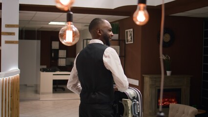Hotel personnel offering luxury services to guest, assisting clients with respect to ensure pleasant stay. Businessman on work trip arriving in lobby, waiting for help with luggage.
