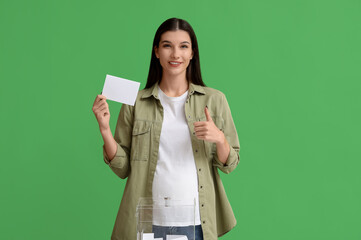 Pregnant woman with voting paper showing thumb-up on green background