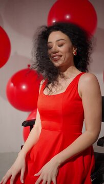 Bright joy in red. Radiant Schumann in red dress sits happily tossing her hair and gazing among red balloons