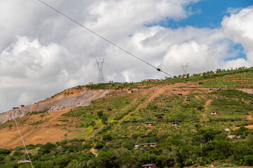 electricity pylons installed in a rural area with houses built on a hill in the background