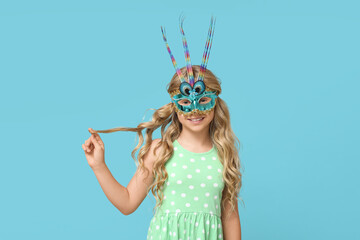 Pretty little girl wearing carnival mask on blue background