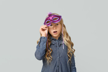 Surprised little girl wearing carnival mask on light background