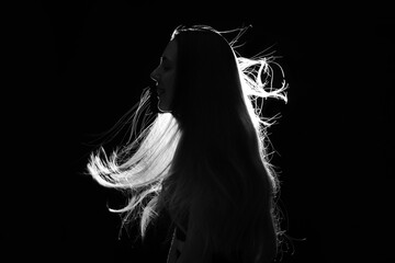 Silhouette of young woman with waving hair on black background