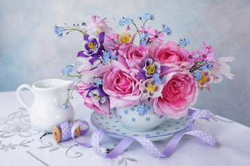 A bouquet of spring and summer flowers in a cup on the table, rose, aquilegia, forget me not flowers, ribbon. Beautiful postcard, still life, blur. - 756043413