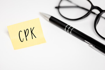 A yellow sticky note on a white background with the handwritten inscription "CPK", next to it a black pen and glasses (selective focus)