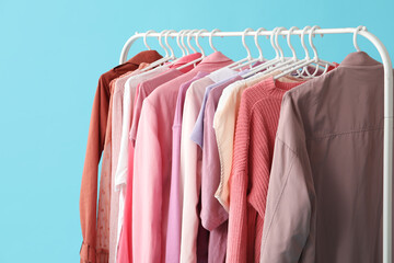 Rack with stylish clothes on blue background, closeup