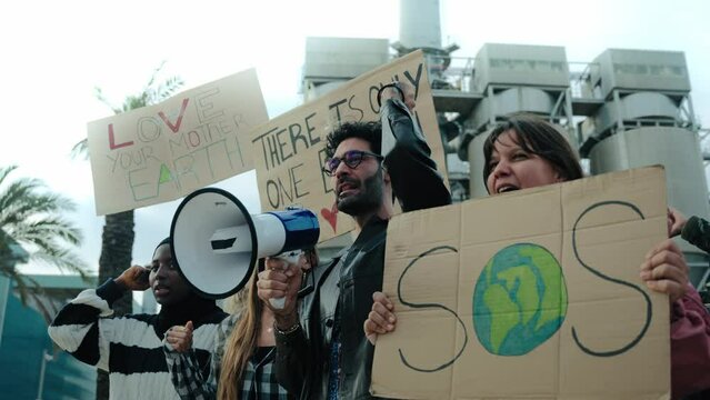 Group of diverse people shouting angrily outdoor manifesting for global warming. Pro-earth demonstration with banners for climate change. Man with megaphone in a protest against pollution in community