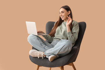 Beautiful young happy woman with laptop resting on comfortable armchair against brown background