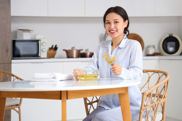 Young Asian woman preparing steam inhalation with herbs at table in kitchen