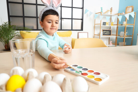 Cute little boy in bunny ears painting Easter eggs at home