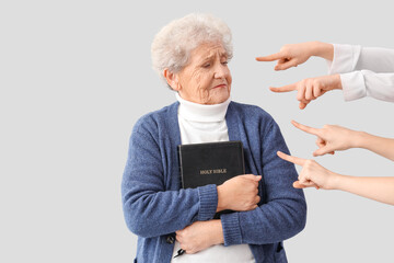 People pointing at senior woman with Holy Bible on light background. Accusation concept