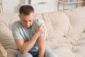 Mature man suffering from shoulder pain at home - obrazy, fototapety, plakaty