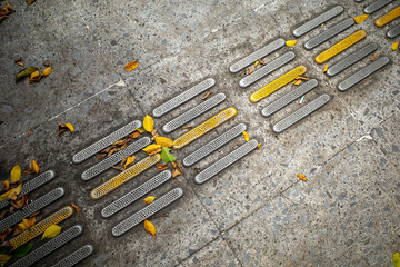 Yellow tactile paving for blind people or visually impaired with dry leaves