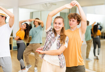 Interested modern teens learning to dance waltz in pairs in choreographic studio .