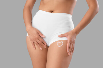 Beautiful young African-American woman with stretch marks on her body and cream in shape of heart against grey background, closeup