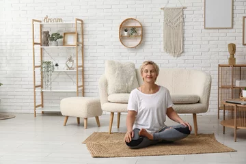 Schilderijen op glas Mature woman meditating while sitting on floor at home © Pixel-Shot