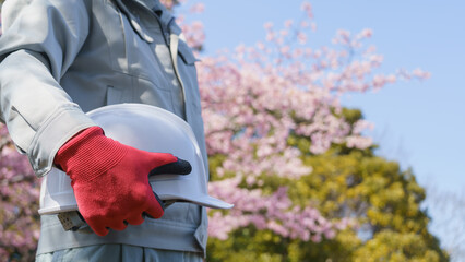 桜の花とヘルメットを持つ作業服の男性