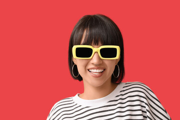 Stylish young woman in sunglasses with nose piercing on red background