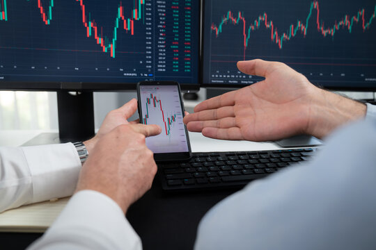 Cropped photo of exchange traders pointing lowest chart stage on dynamic graph with smartphone on hands focus, analyzing comparing with monitor and phone, discussing financial technology. Sellable.