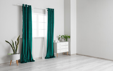 Stylish green curtains with houseplants and chest of drawers in living room