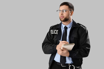 Male police officer with notebook on grey background